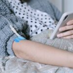 A woman receiving intravenous therapy for cancer treatment while using her phone, symbolizing connection and hope.