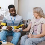 Volunteer checking elderly woman's blood pressure at home. Compassionate healthcare support.