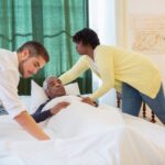 Caregivers supporting an elderly man lying in bed, providing assistance and comfort.